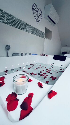 A modern bathroom with a bathtub, a glass candle, and rose petals on the floor. - Lar de Canedo (Carnota)
