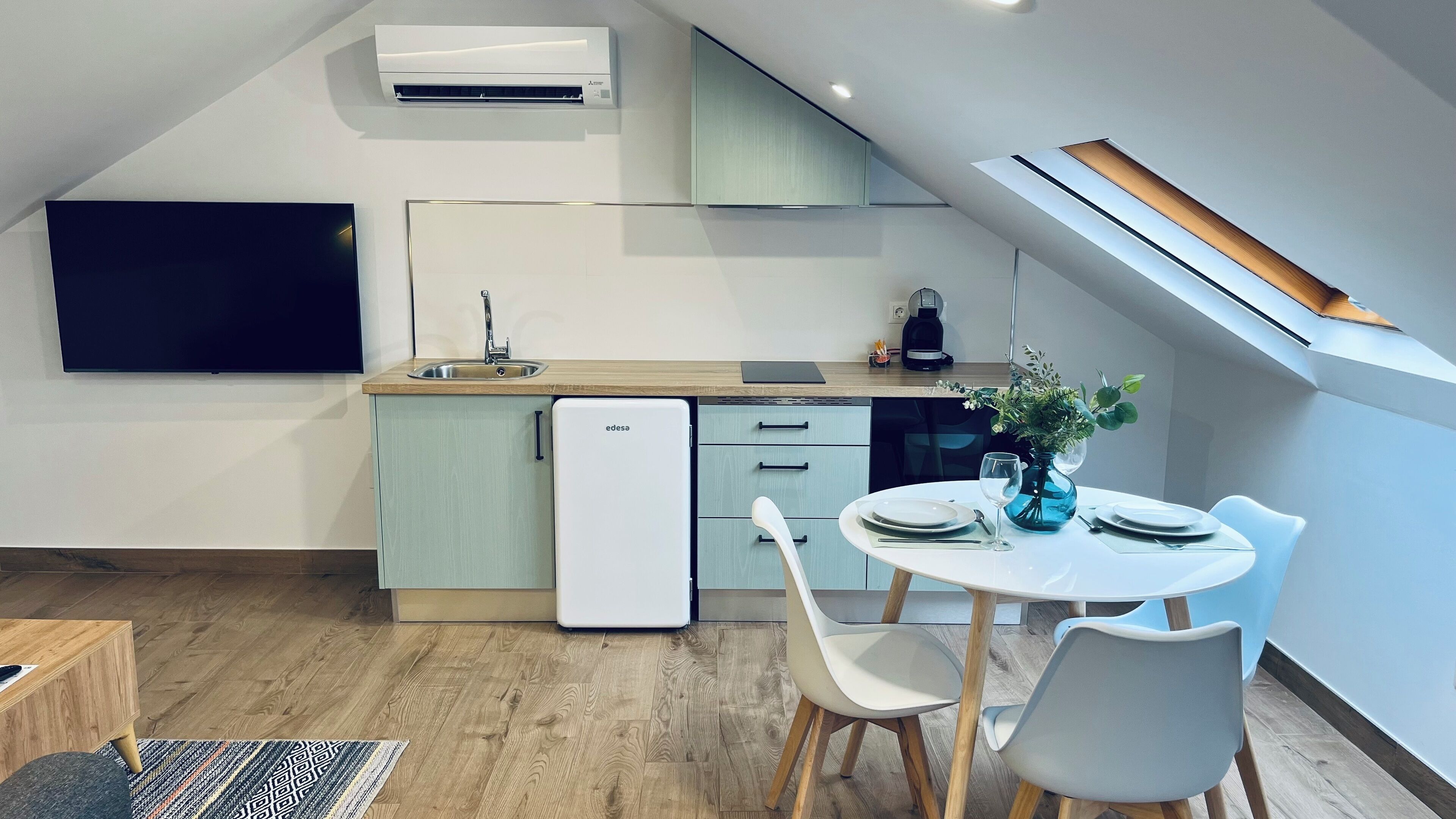 A modern kitchen with a built-in dishwasher, a dining area with a round table and chairs, and a skylight above the kitchen.