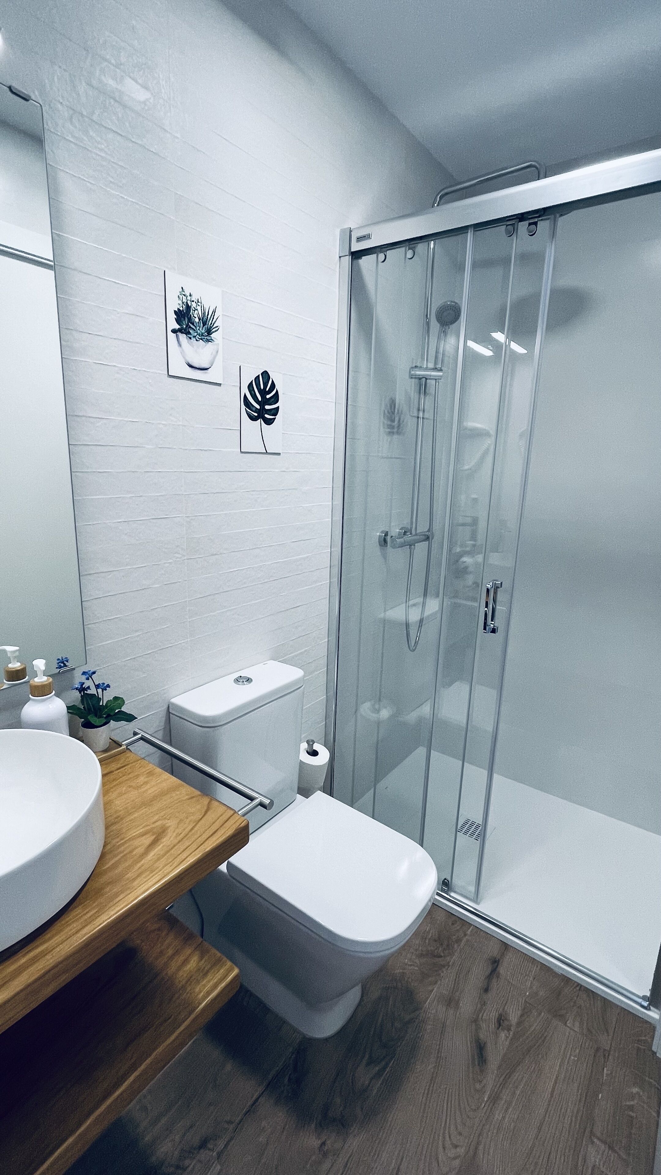 A modern bathroom with a glass shower enclosure, a wooden vanity, and a toilet.