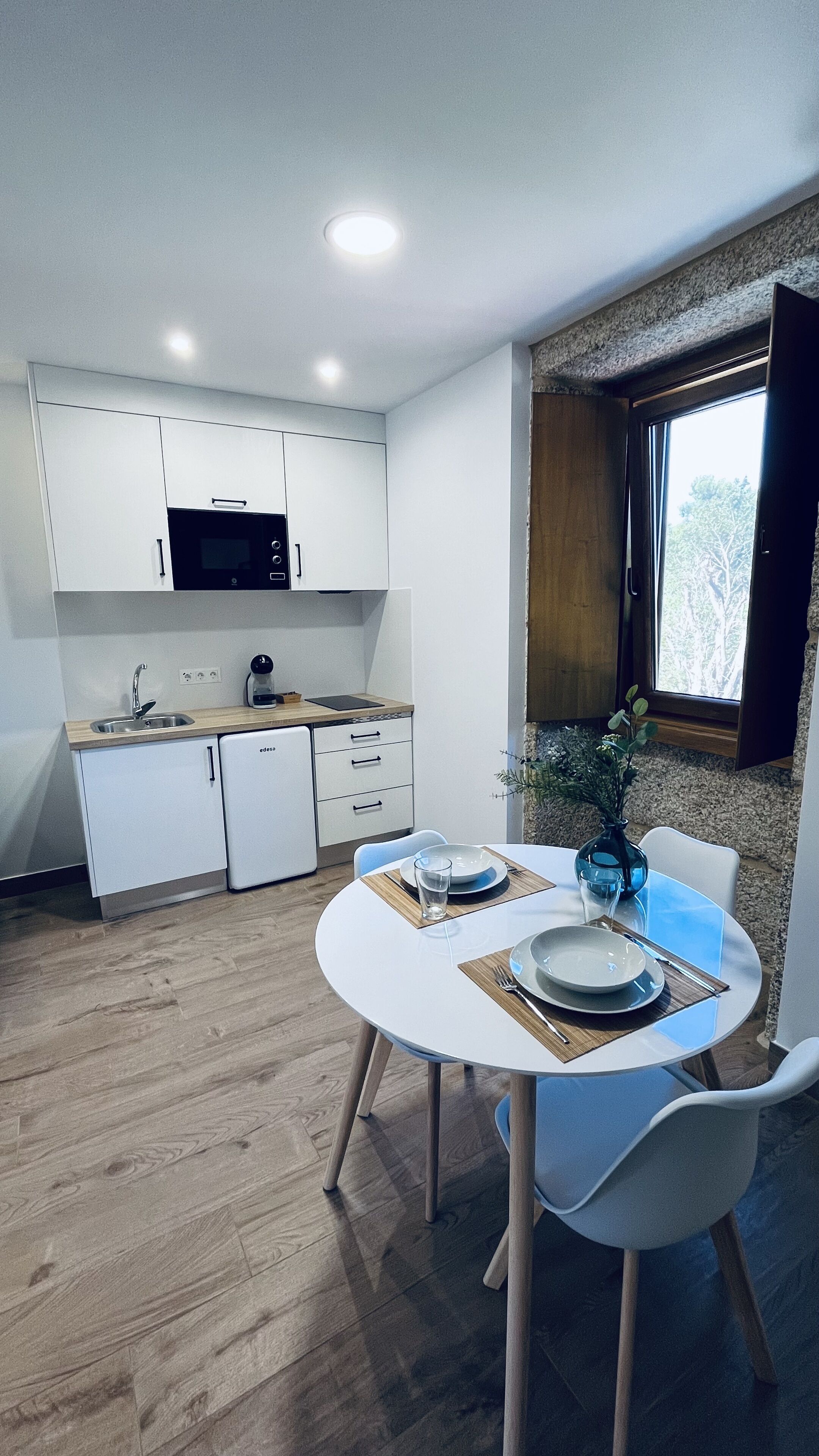 Una cocina moderna con armarios blancos, horno empotrado y ventana con vistas a árboles.