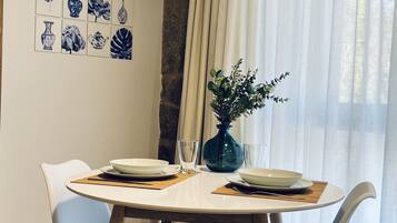Un comedor con una mesa redonda, dos sillas, un florero con flores y decoración en la pared.