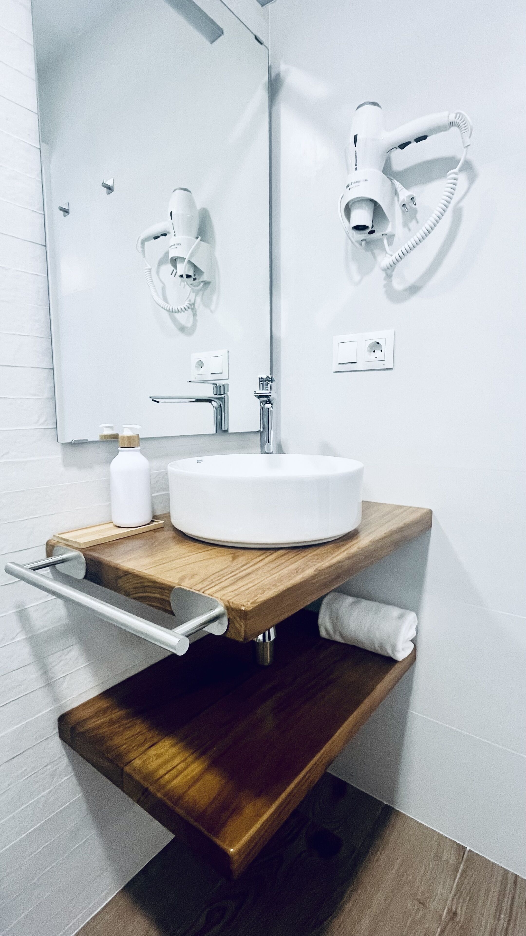Une salle de bain moderne avec un lavabo blanc, un meuble-lavabo en bois, un miroir, un sèche-cheveux et un porte-serviettes.
