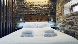 Una habitación con pared de piedra, cabecera de madera y cama con ropa de cama y toallas blancas.