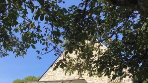 A stone building with a red door, a covered outdoor seating area with plastic chairs, and a large umbrella providing shade. - In the countryside, beaches just a few minutes away... (Plomeur)
