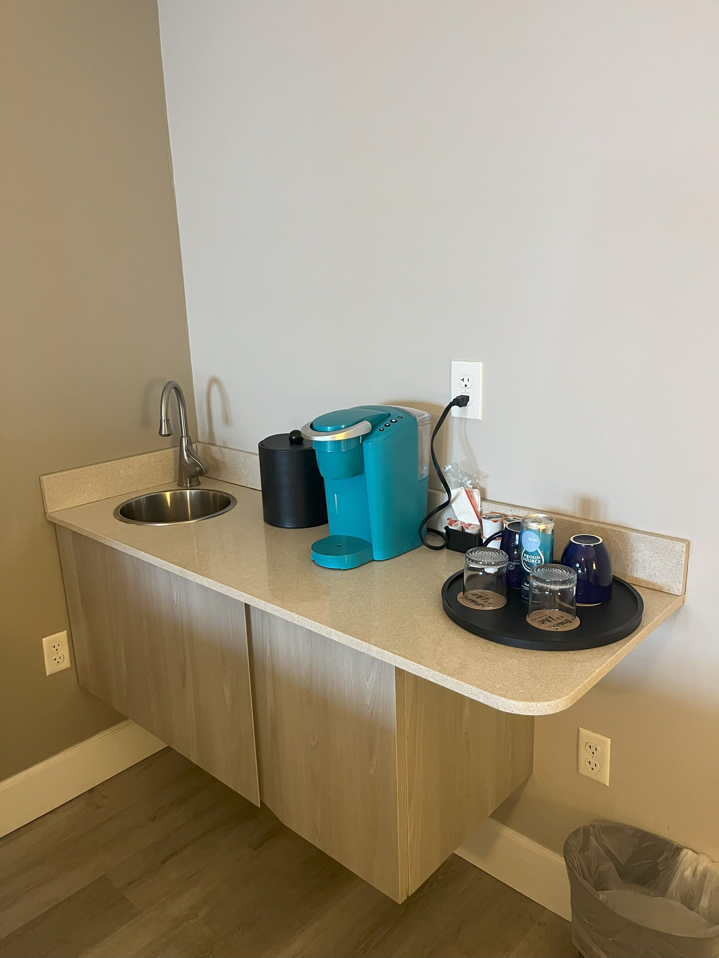 A kitchen with a sink, a coffee maker, and a trash bin.
