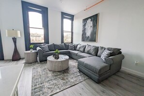 A modern living room with a grey sectional sofa, two round coffee tables, a patterned rug, and a large window with a city view. - 3A Unique Aptmt in Easton`s Heart (Easton)