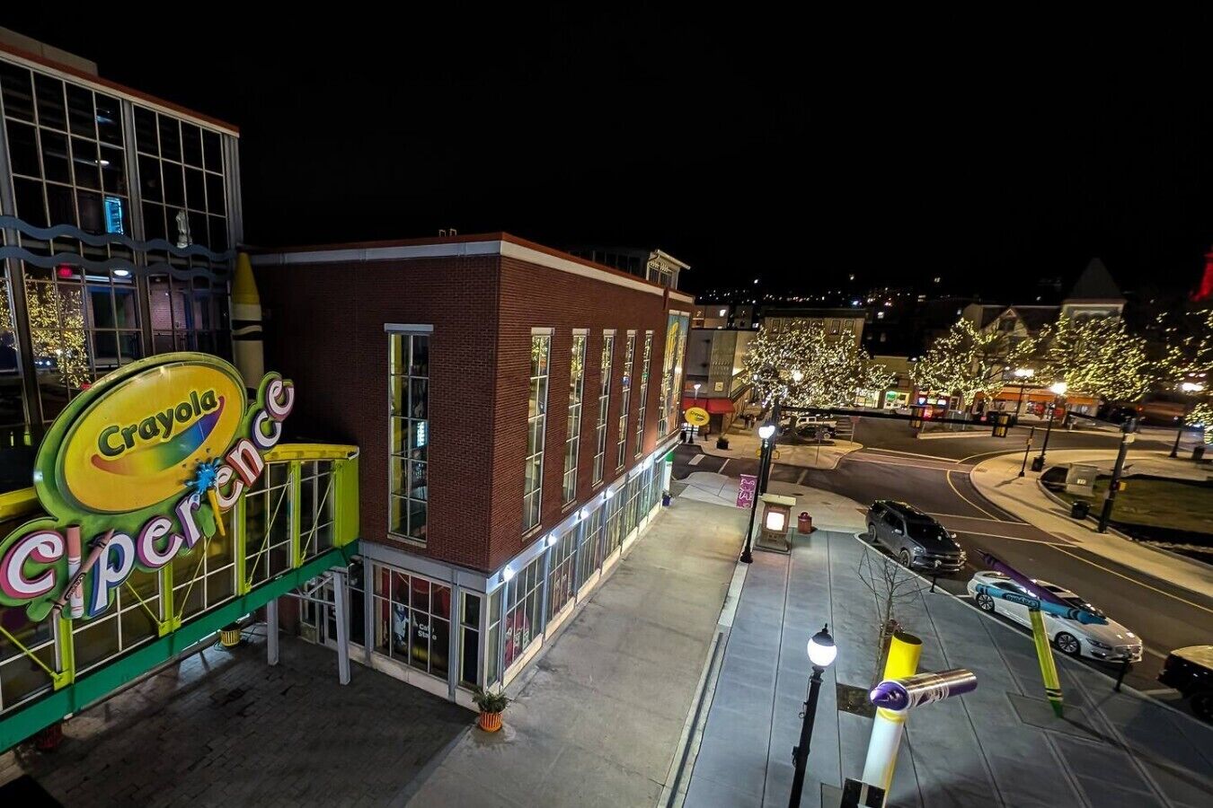 Een Crayola Experience winkel bij nacht, met een gebouw van baksteen, een groen luifel en een parkeerplaats met auto's.