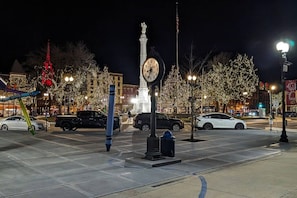 A public square with a clock, trees, and cars.
