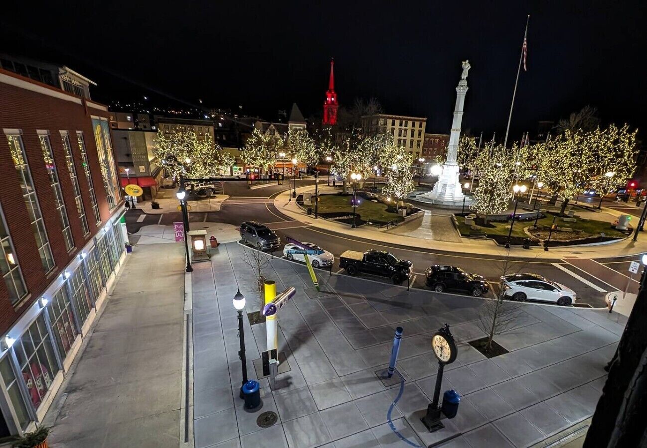 A nighttime urban square with a monument, street lamps, and a clock.