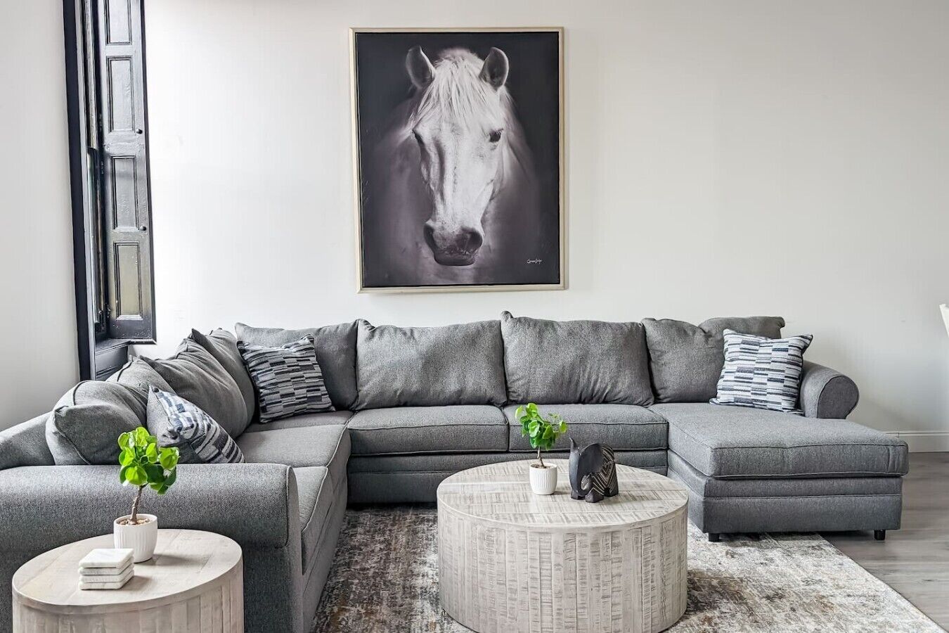 Ein modernes Wohnzimmer mit einem grauen Ecksofa, einem runden Couchtisch und einem gerahmten Bild eines Pferdes an der Wand.