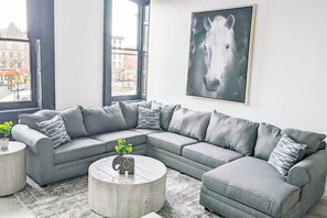 A modern living room with a grey sectional sofa, a round coffee table, and a cityscape view through large windows. - 3A Unique Aptmt in Easton`s Heart (Easton)