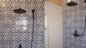 Un baño con baldosas estampadas, una ducha con cabezal de ducha manual e iluminación empotrada en la pared.