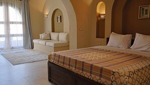 A bedroom with a large bed, a sofa, and a window with curtains. - Malkata House - 32 ppl - Desert Oasis: Pool & Dine (Luxor)