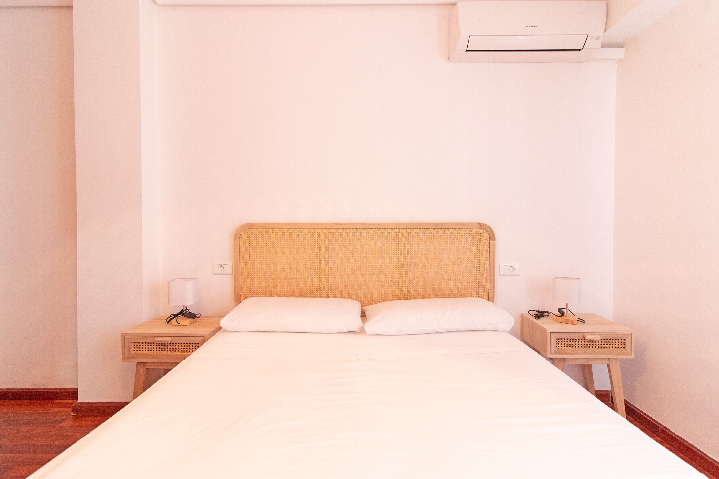 Une chambre simple et bien rangée, avec un lit, deux tables de chevet et un appareil de climatisation.