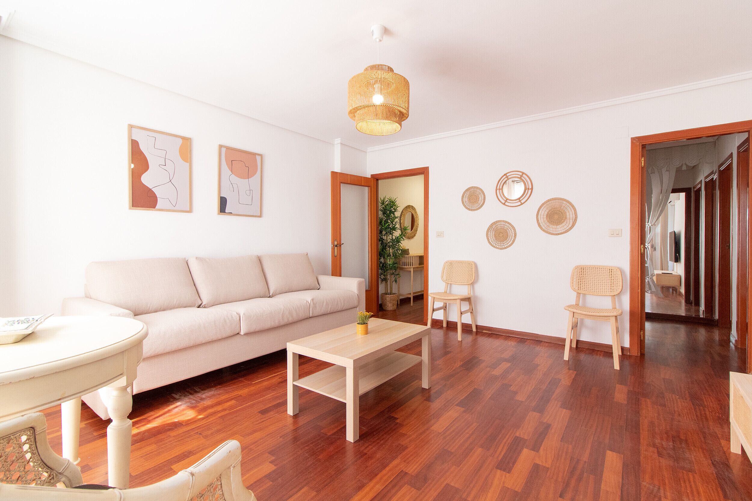 A living room with a sofa, a coffee table, and two chairs. There are wall decorations and a door leading to another room.