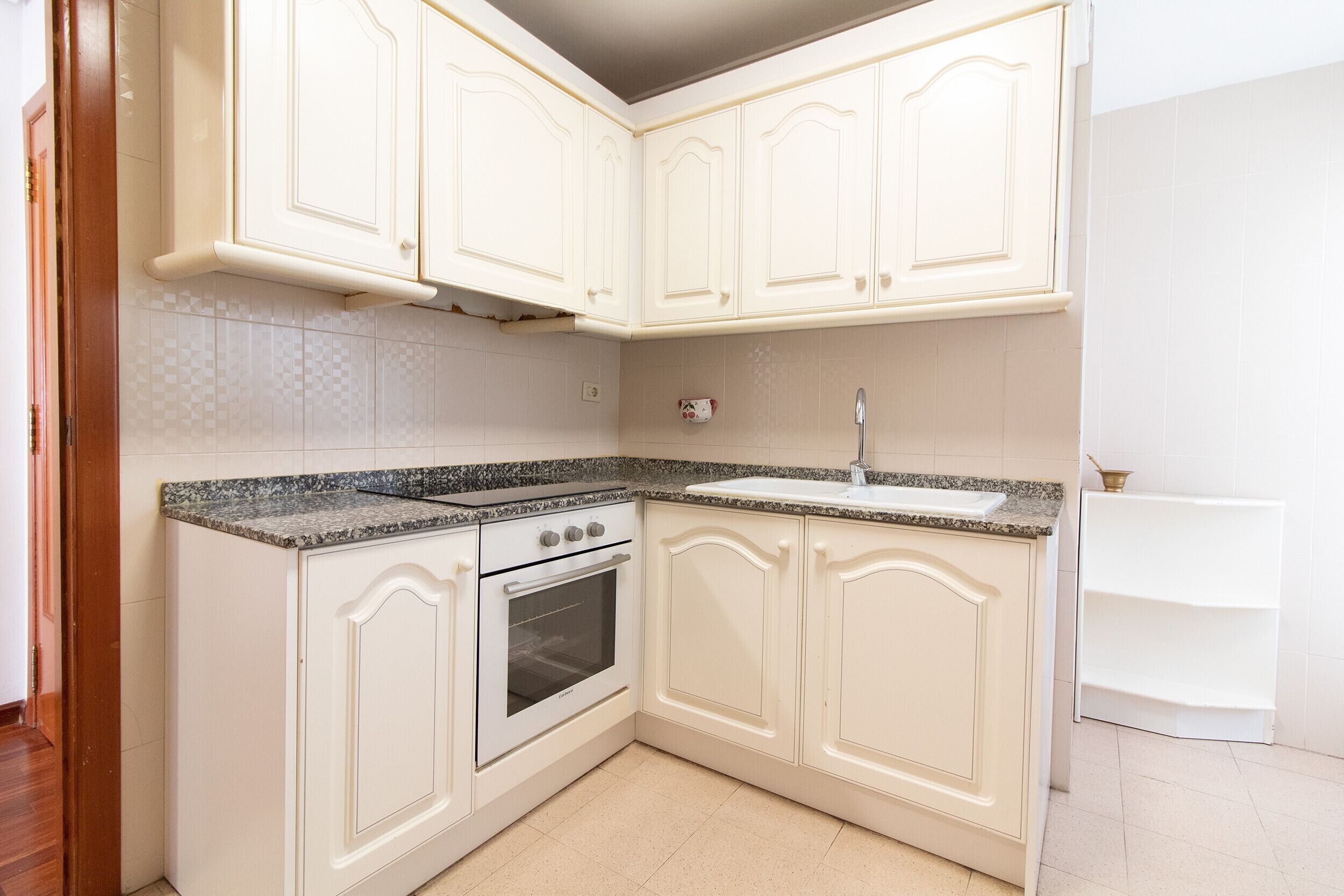 A kitchen with white cabinetry, a built-in oven, a granite countertop, and a sink.