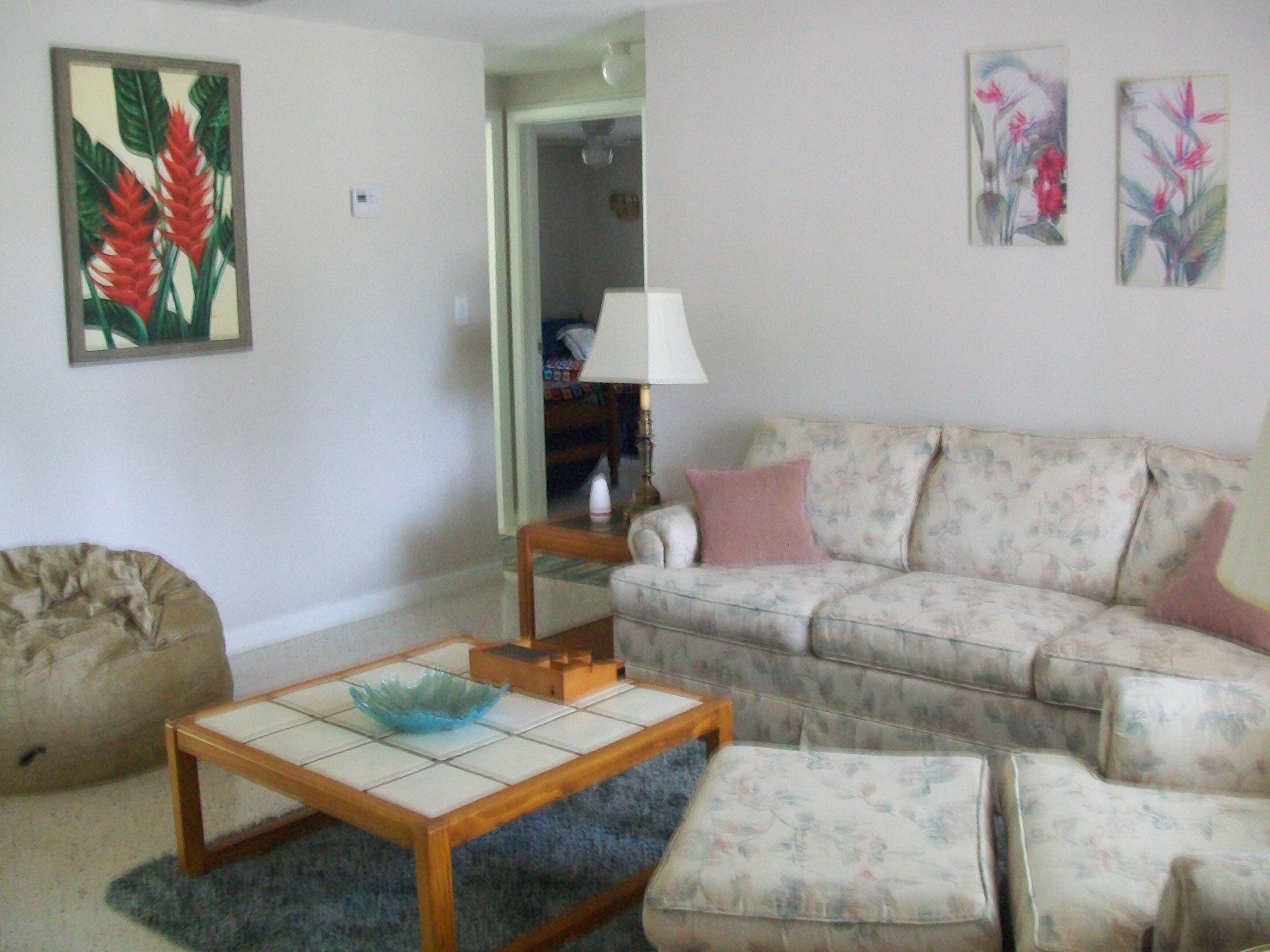 A living room with a sofa, a small table, and a bean bag chair. There are two paintings on the wall.