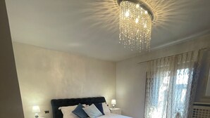 Een slaapkamer met een groot bed, een kroonluchter, een nachtkastje en een raam met gordijnen.