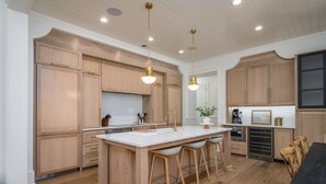A modern kitchen with wooden cabinets, a central island with bar stools, pendant lighting, and built-in appliances. - Gorgeous new luxury beach house - be the first to experience this dream home! (Hilton Head)