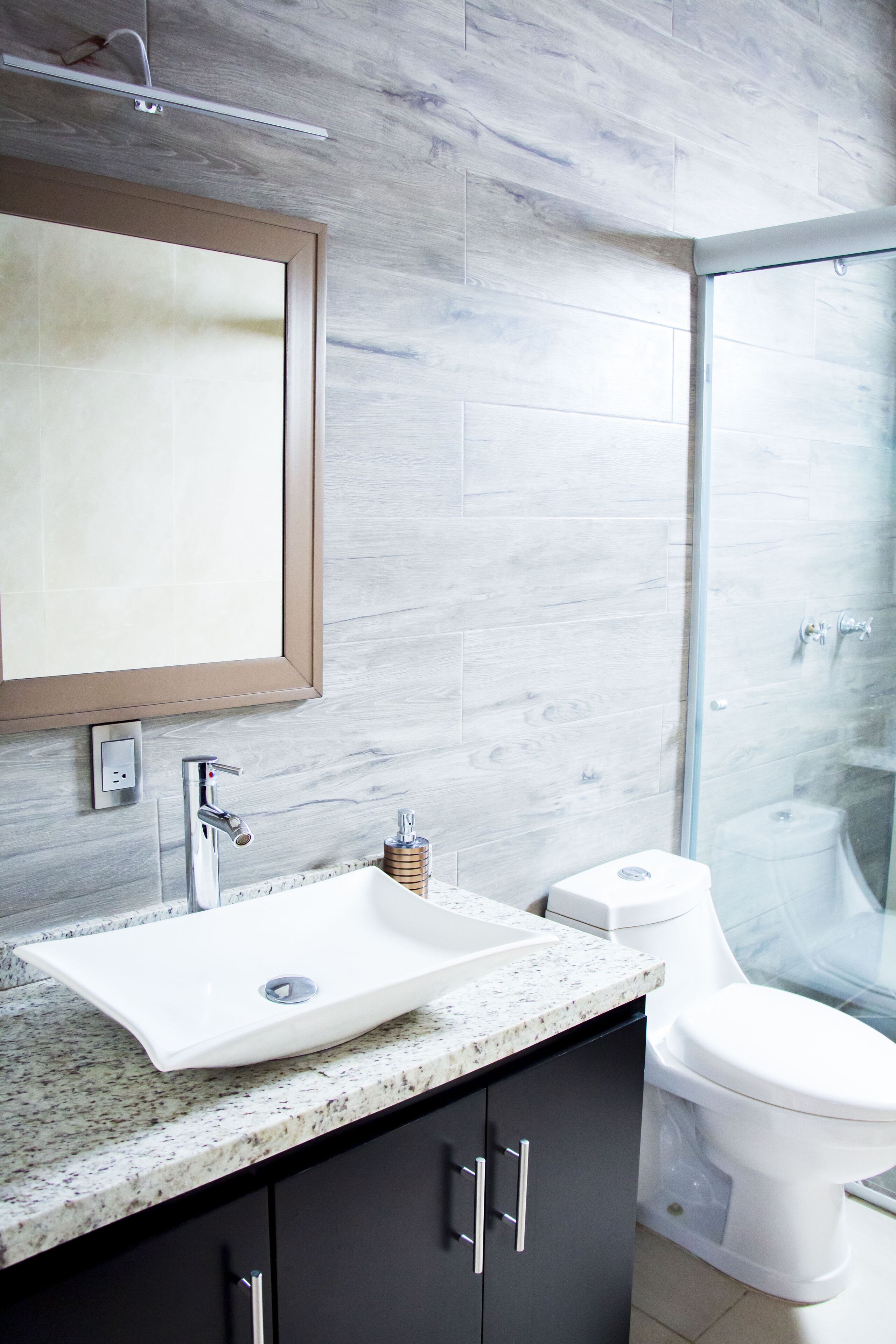 Un baño moderno con un espejo grande, un lavabo, un inodoro y una cabina de ducha de vidrio.