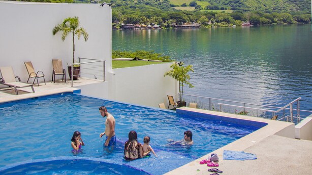 A swimming pool with people, surrounded by a view of a lake and hills.