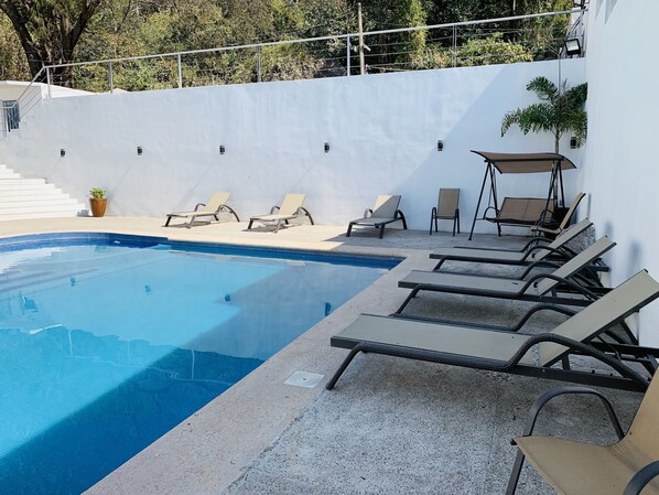 Una piscina con sillas de descanso y una zona de estar techada.