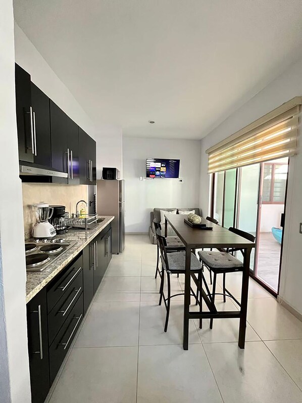 Una cocina moderna con armarios oscuros, estufa empotrada y una zona de comedor con mesa y sillas.