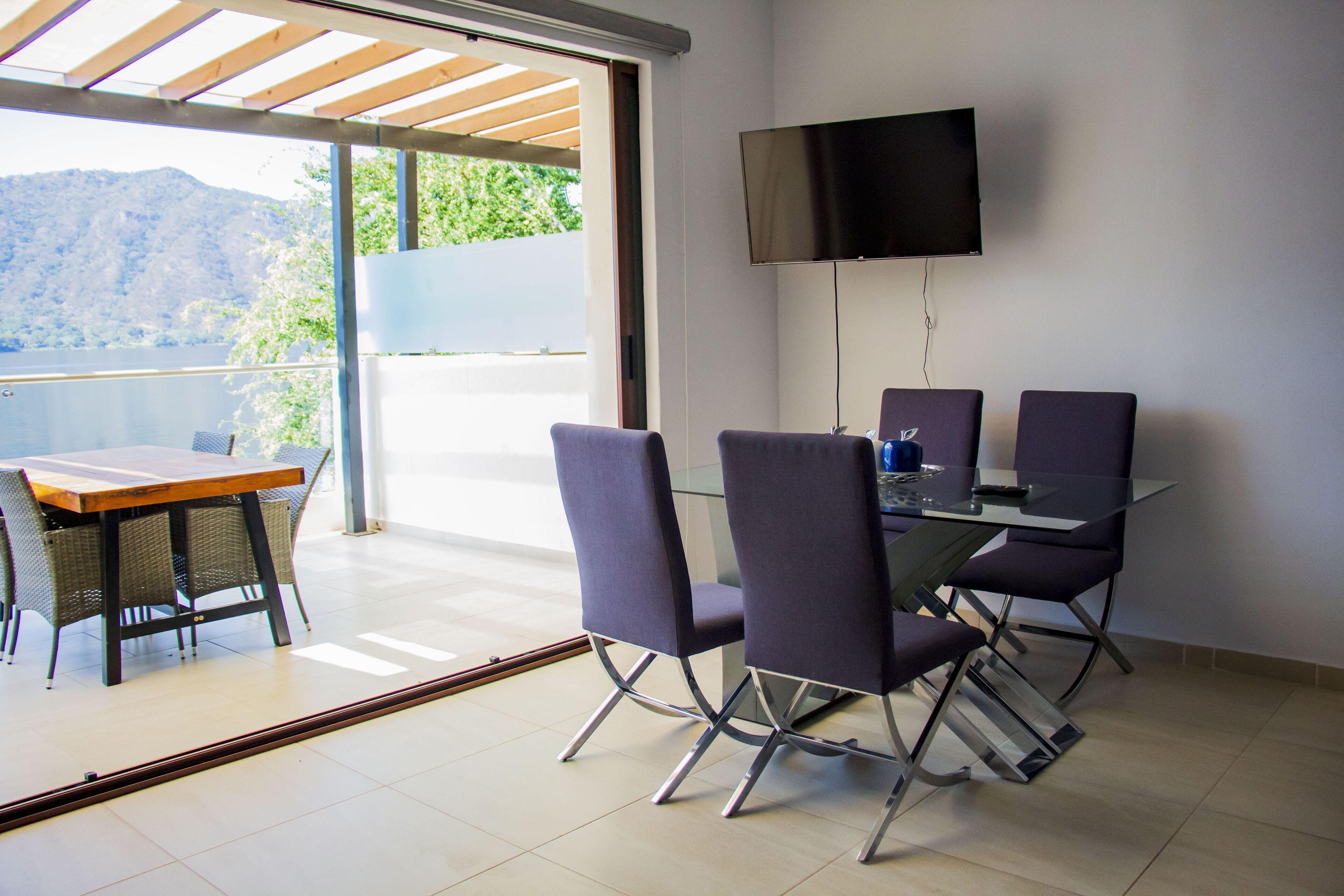 Un espace repas comprenant une table et des chaises, un téléviseur fixé au mur et une vue sur l’extérieur.