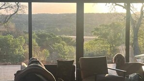 Een kamer met een groot raam dat uitkijkt op een landschap. Er staan twee stoelen en een klein tafeltje.
