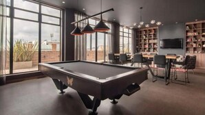 Een modern overdekt zwembad met een pooltafel, zitplaatsen en een boekenkast.