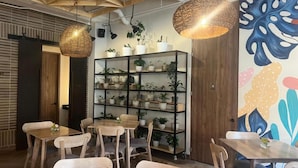 Een gezellig café-interieur met houten tafels en stoelen, een zwarte wandplank vol met potplanten en een levendige abstracte muurschildering.