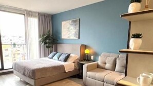 Een moderne slaapkamer met een bed, een bank, een bureau en een groot raam.