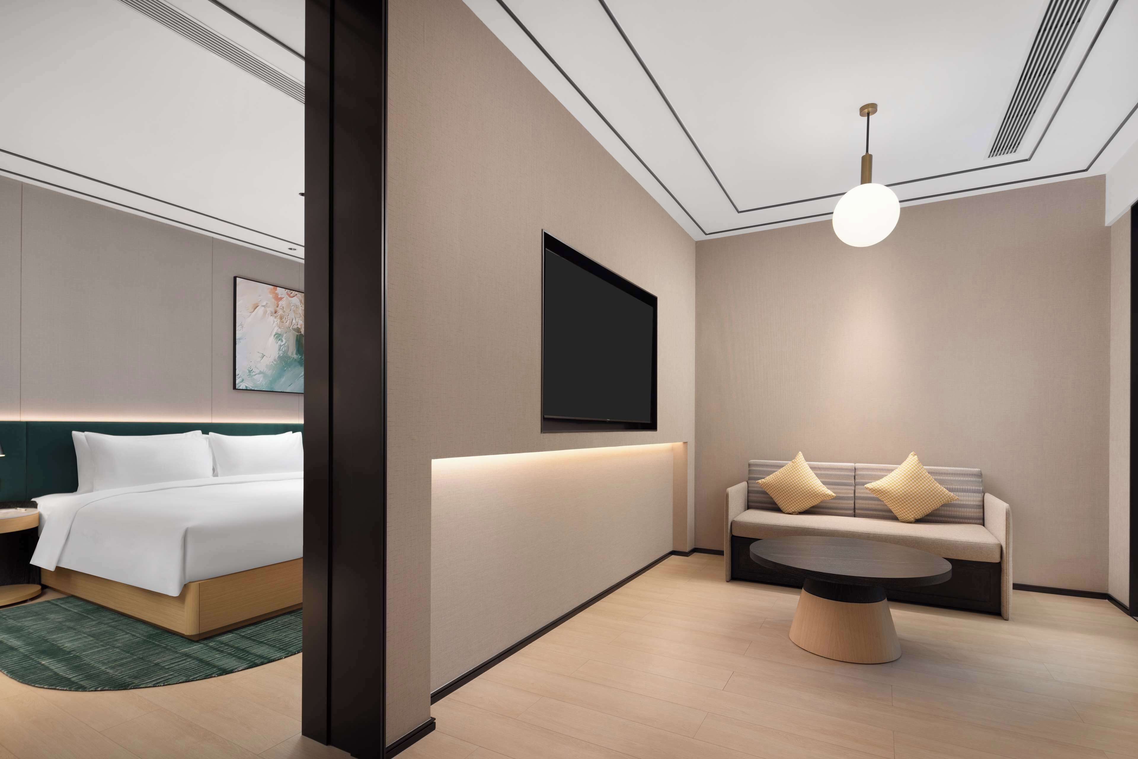 A modern hotel room with a bed, a sofa, a coffee table, and a flat-screen TV mounted on the wall.