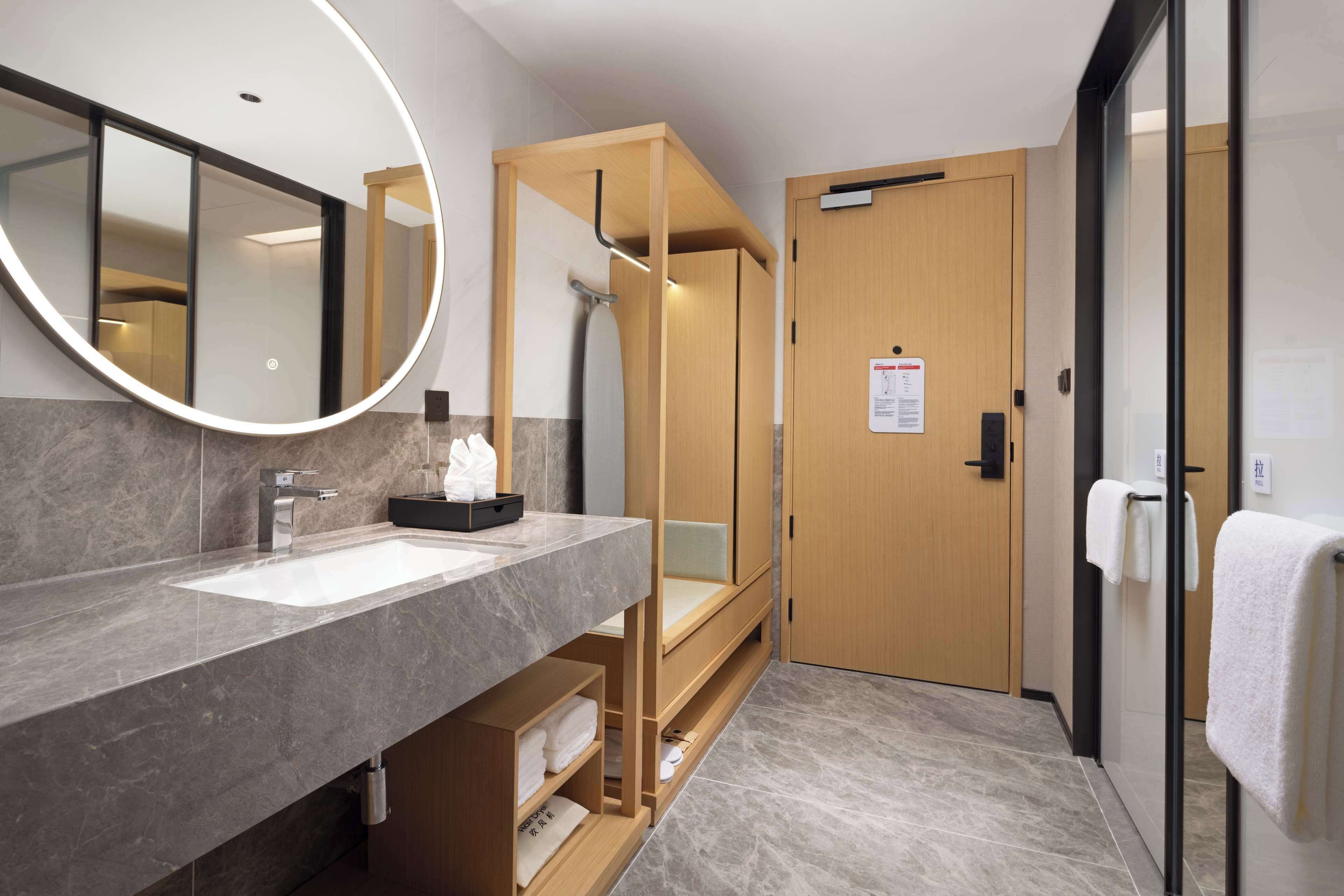 A modern bathroom with a double sink, a large mirror, a shower area, and a wooden door.