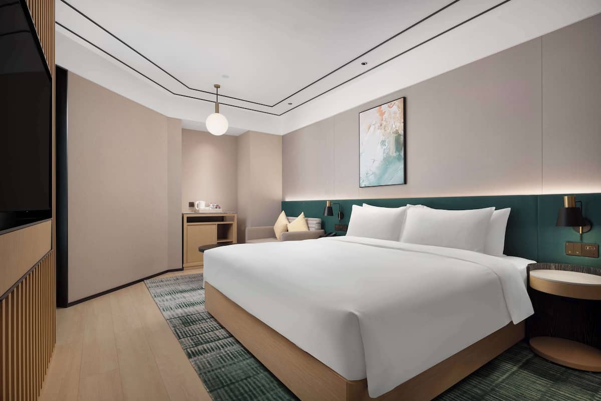 Une chambre d’hôtel moderne, dotée d’un grand lit, d’un bureau, d’une tél évision et d’un tableau au mur.