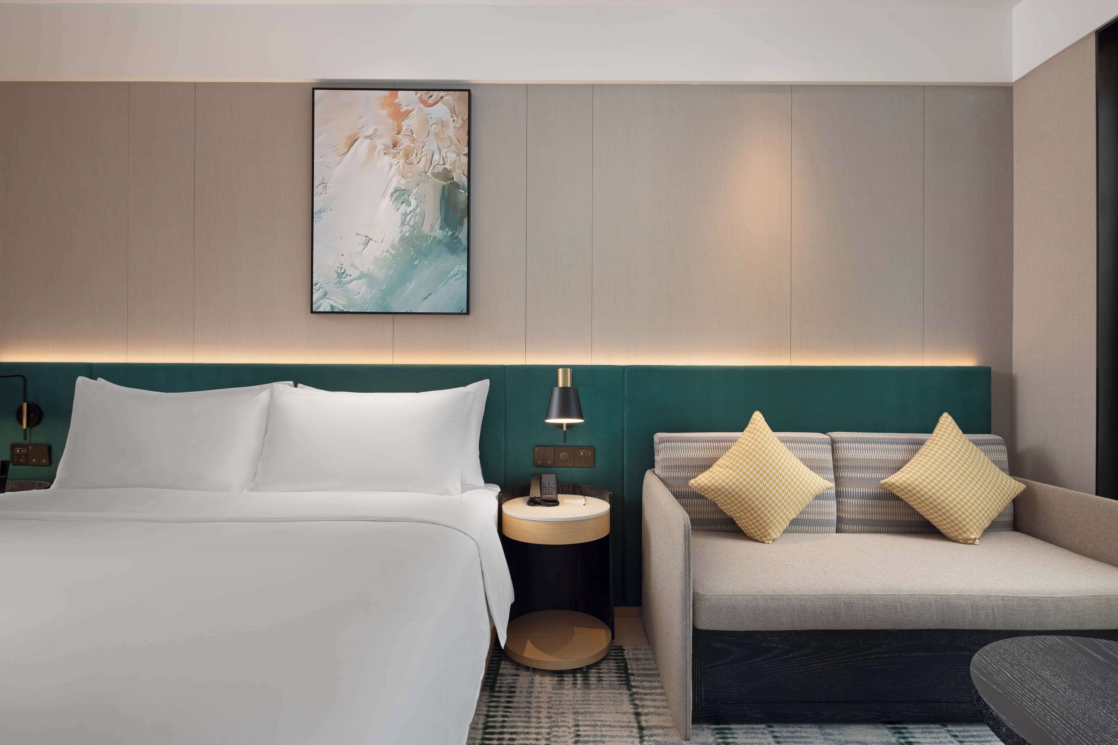 Une chambre d’hôtel comprenant un lit, un canapé, une table de chevet avec une lampe et une œuvre d’art accrochée au mur.