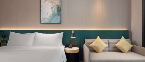 Une chambre d’hôtel comprenant un lit, un canapé, une table de chevet avec une lampe et une œuvre d’art accrochée au mur.