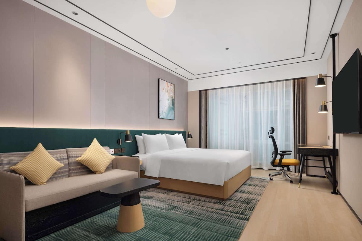 Une chambre d’hôtel moderne équipée d’un lit, d’un canapé, d’un bureau et d’une grande fenêtre avec des rideaux.