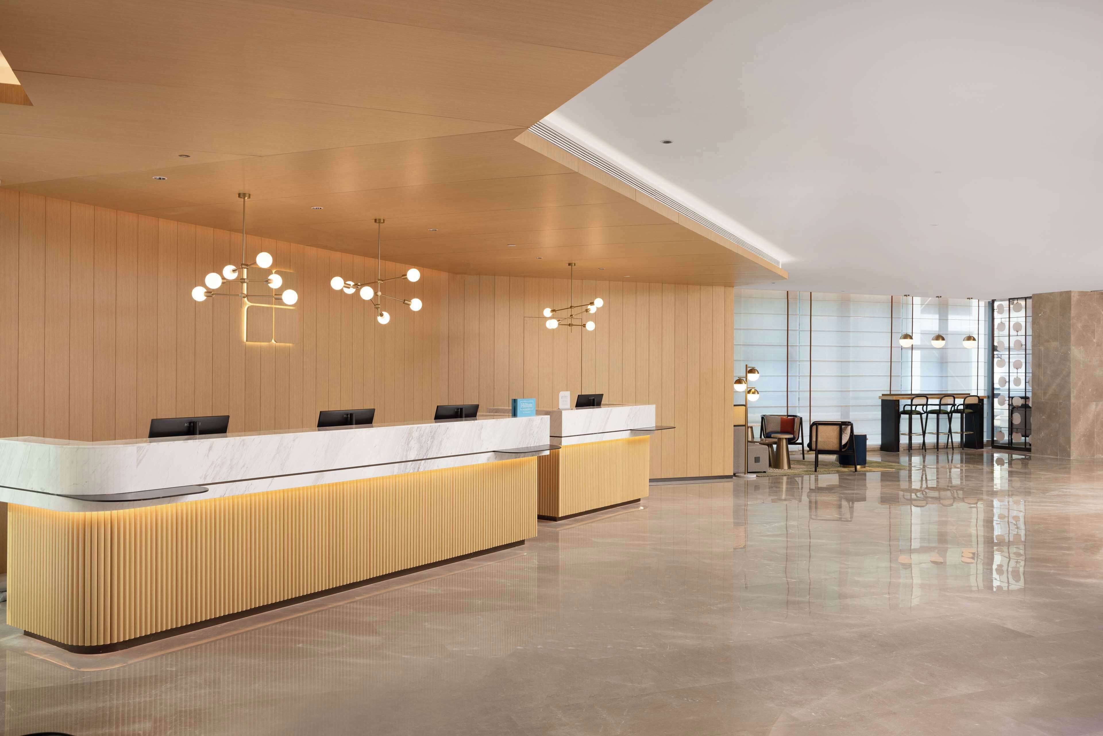 A modern reception area with a wooden reception desk, a glass partition, and a seating area with chairs.