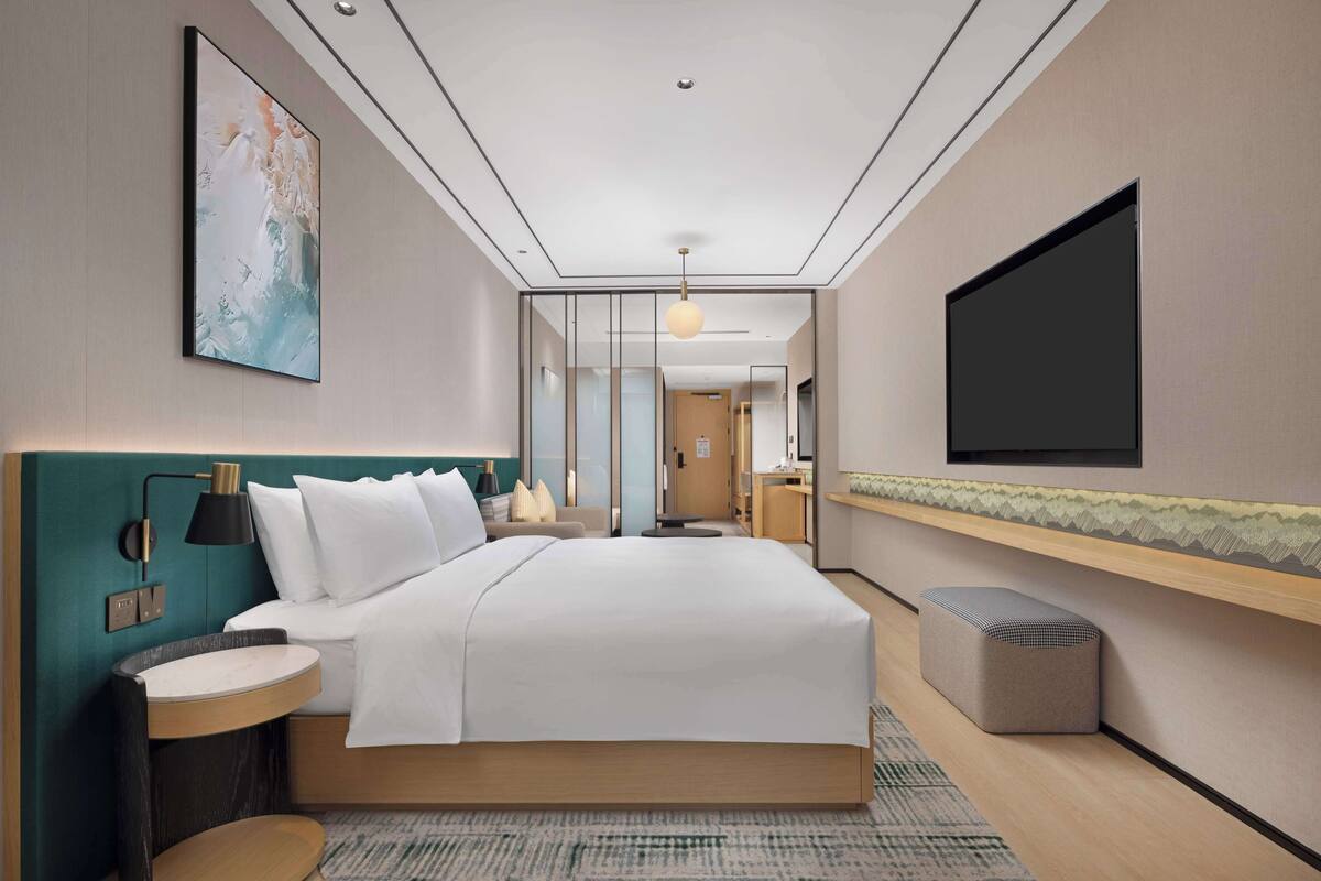 Une chambre d’hôtel moderne, dotée d’un grand lit, de tables de chevet, d’un téléviseur et donnant sur le couloir.