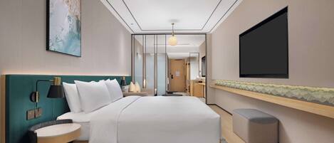 Quarto de hotel moderno com uma cama grande, mesas de cabeceira, uma TV e vista para o corredor.