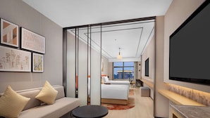 Una habitación de hotel moderna con sofá, una mesa redonda, cama y vistas a la ciudad a través de amplias ventanas.
