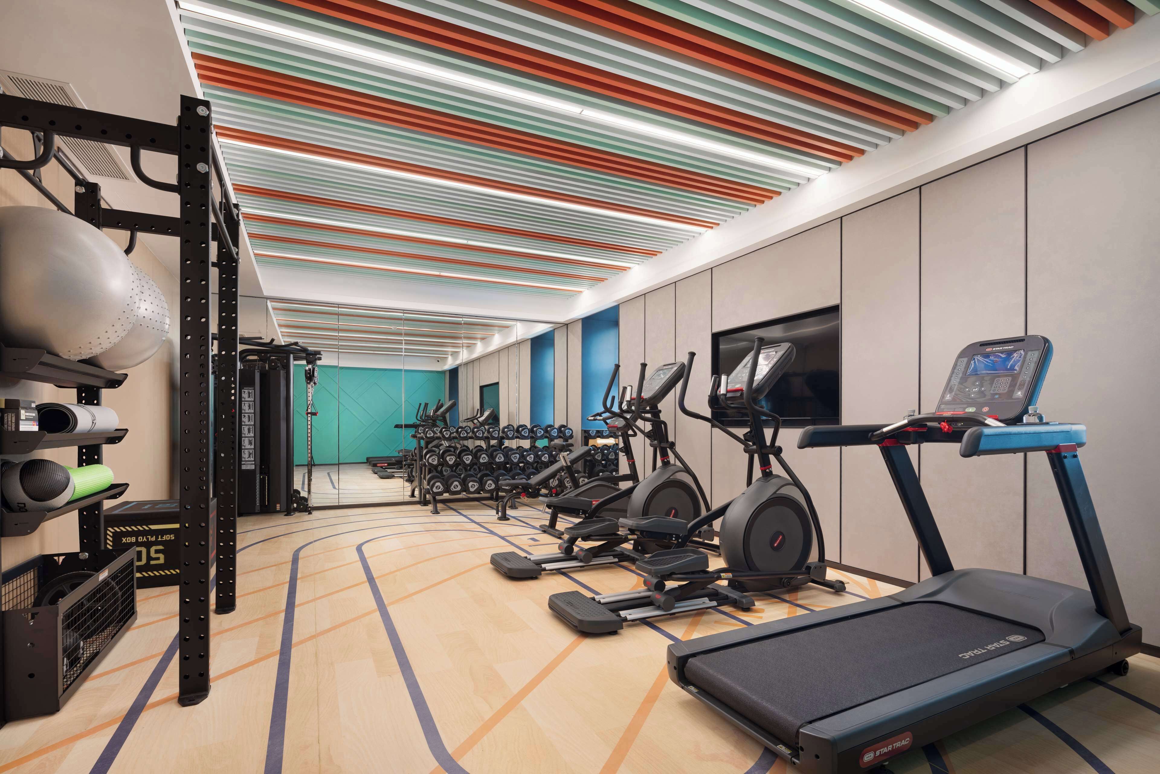 A modern gym with treadmills, elliptical machines, and weightlifting equipment.