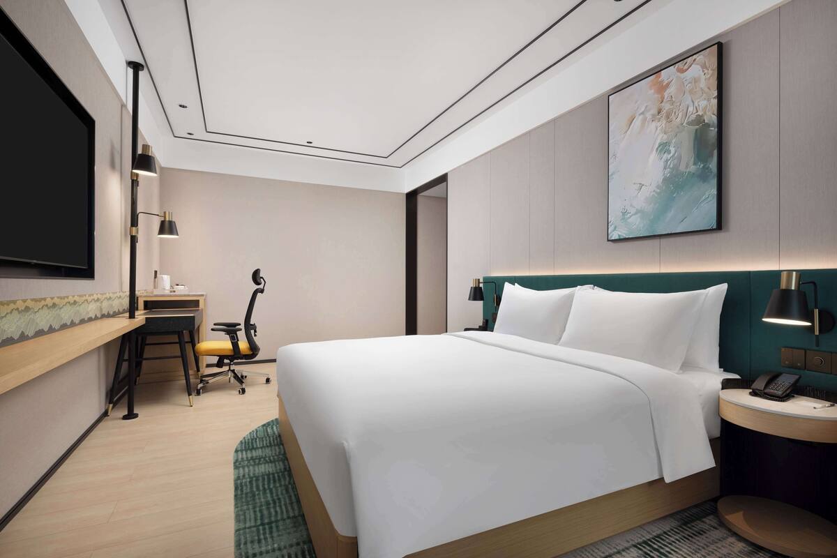 Une chambre d’hôtel moderne, dotée d’un grand lit, d’un bureau, d’une chaise, d’un téléviseur à écran plat et d’un tableau au mur.
