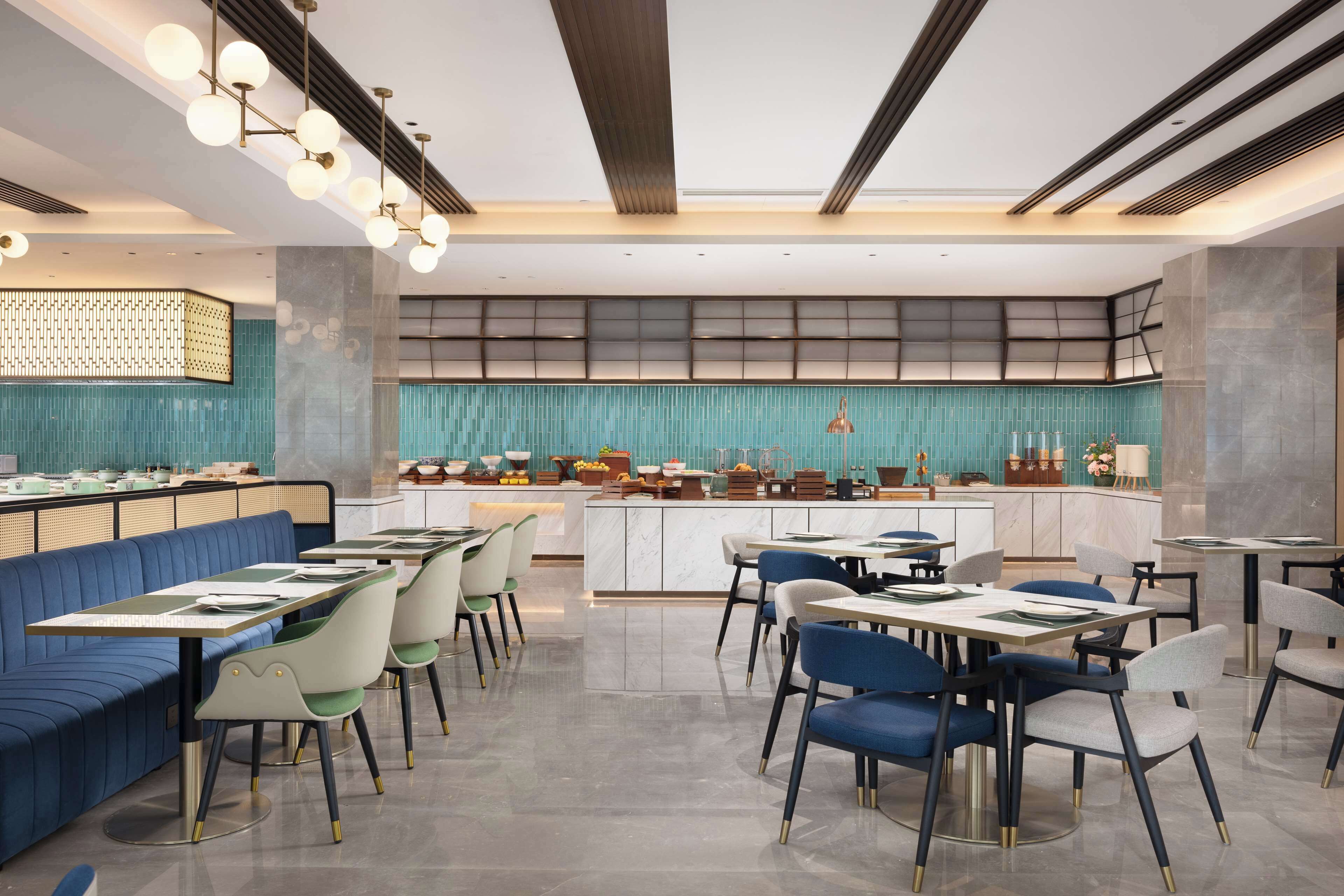 A modern restaurant with a central bar, seating areas, and a teal-colored wall.