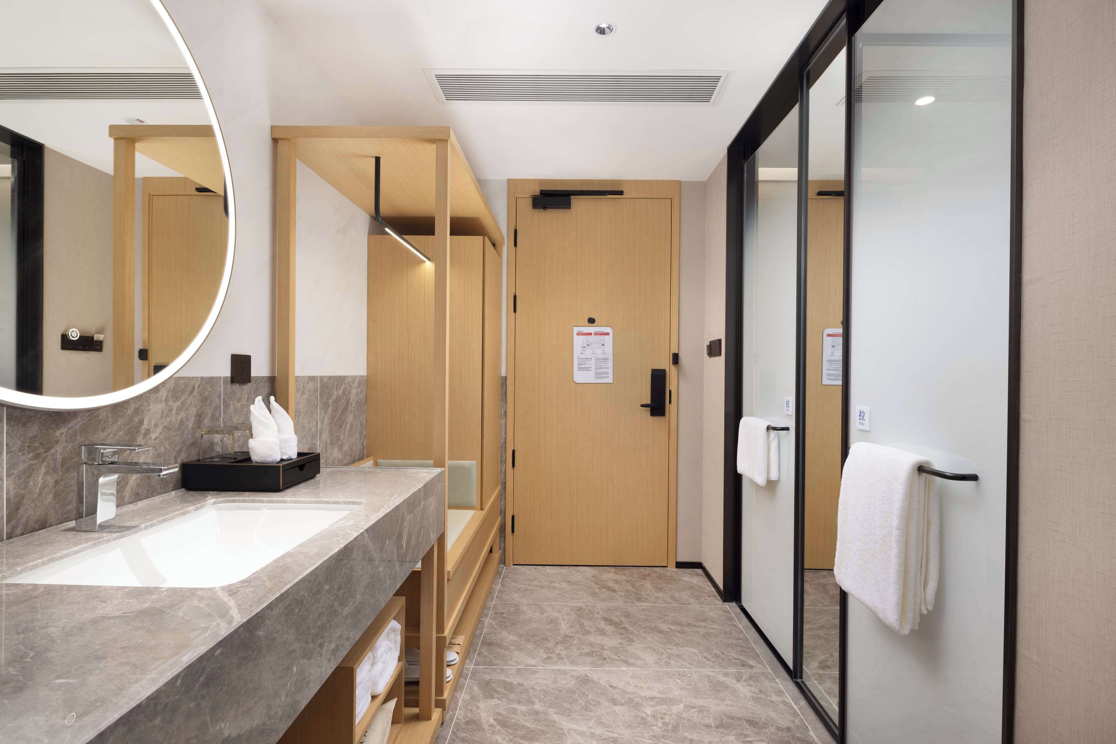 A modern bathroom with a marble sink, wooden vanity, and a large mirror.