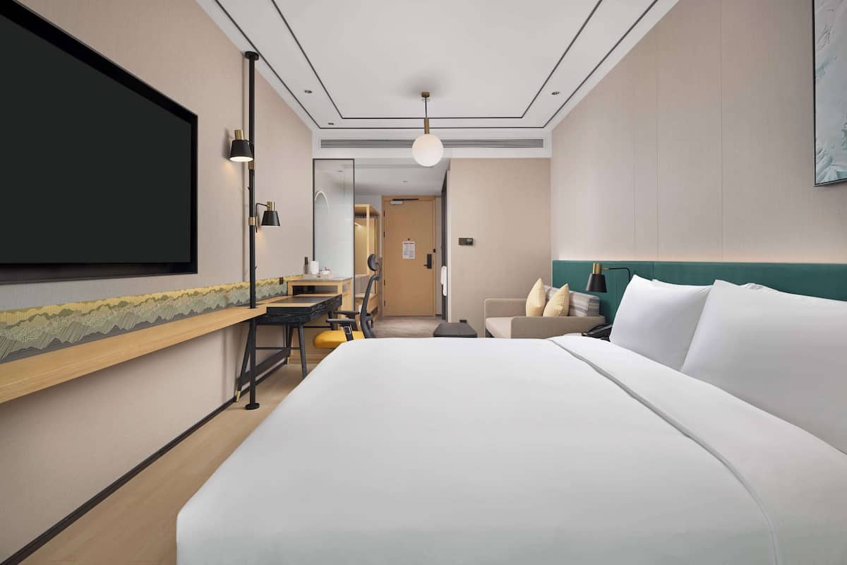 Une chambre d’hôtel avec un grand lit, un bureau, une chaise, une télévision et une lampe.