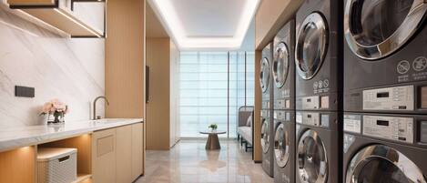 Lavandería moderna con varias lavadoras, encimera de mármol y vistas al exterior a través de amplias ventanas.