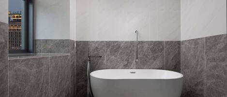 A modern bathroom with a freestanding bathtub, a shower, and a large window offering a city view.