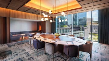 A modern conference room with a round table, comfortable seating, and large windows offering city views.
